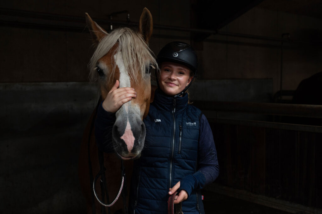 Elev fra Ølgod Efterskole står sammen med en brun hest i stalden.