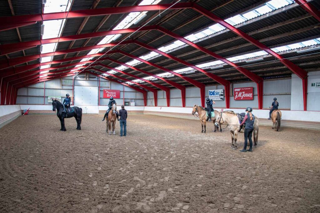Elever fra Ølgod Efterskole rider på heste under undervisning i en stor ridehal.